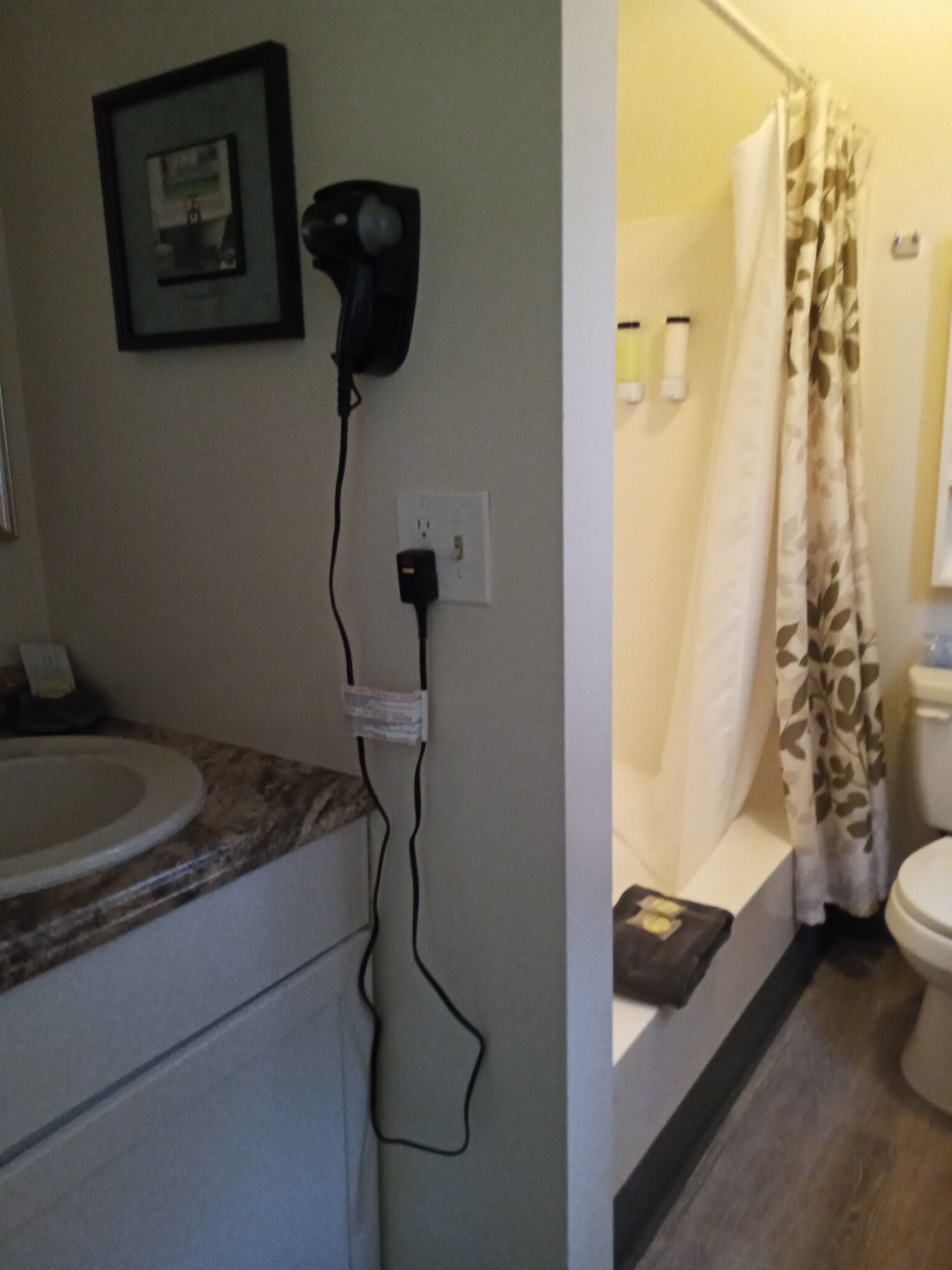 Une salle de bain équipée d’un lavabo, d’un sèche-cheveux fixé au mur, d’un rideau de douche et d’un présentoir mural pour les articles de toilette.