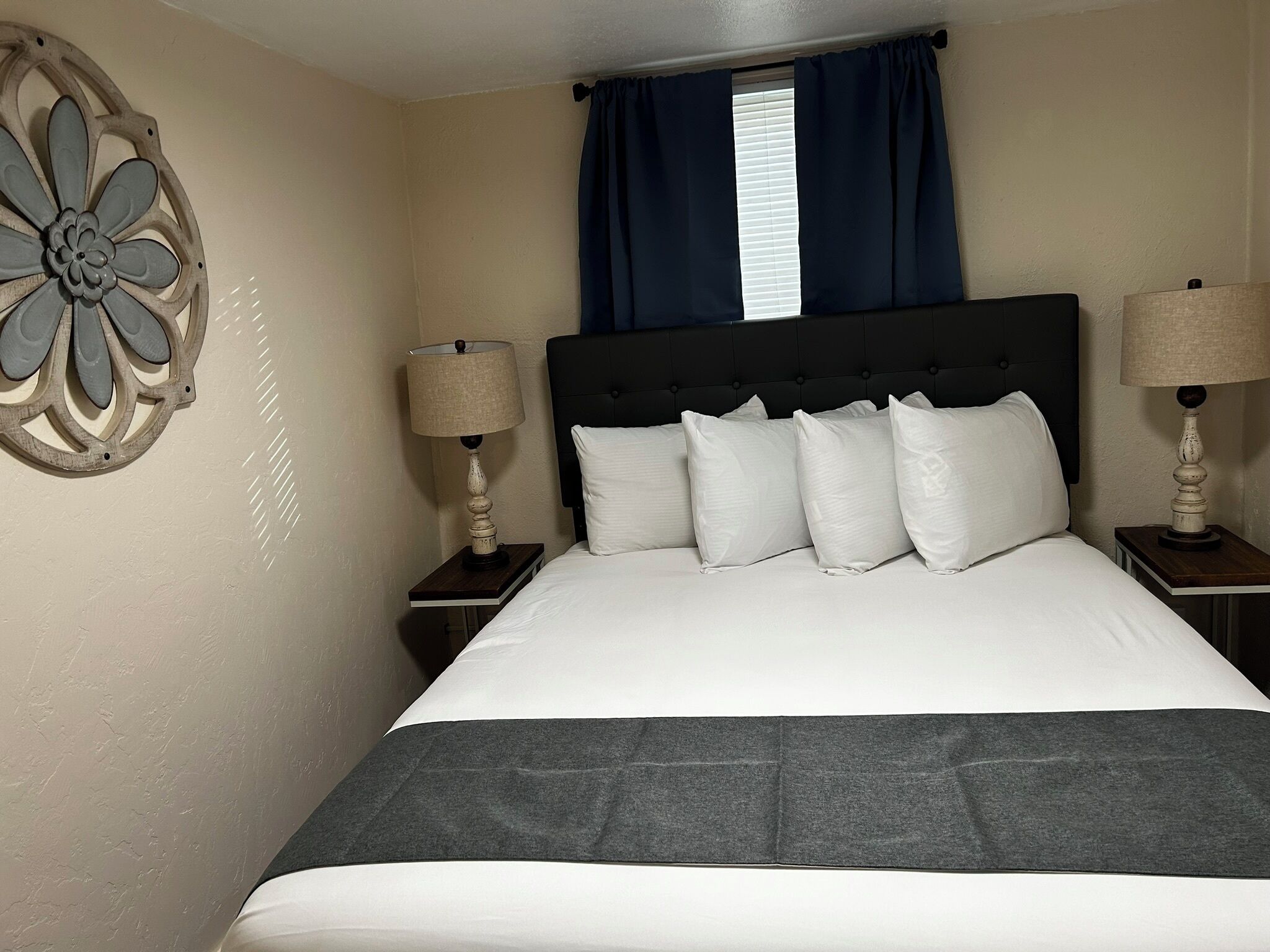 A neatly made bed with white linens and a dark gray throw blanket. There are two bedside tables with lamps and a decorative wall piece.