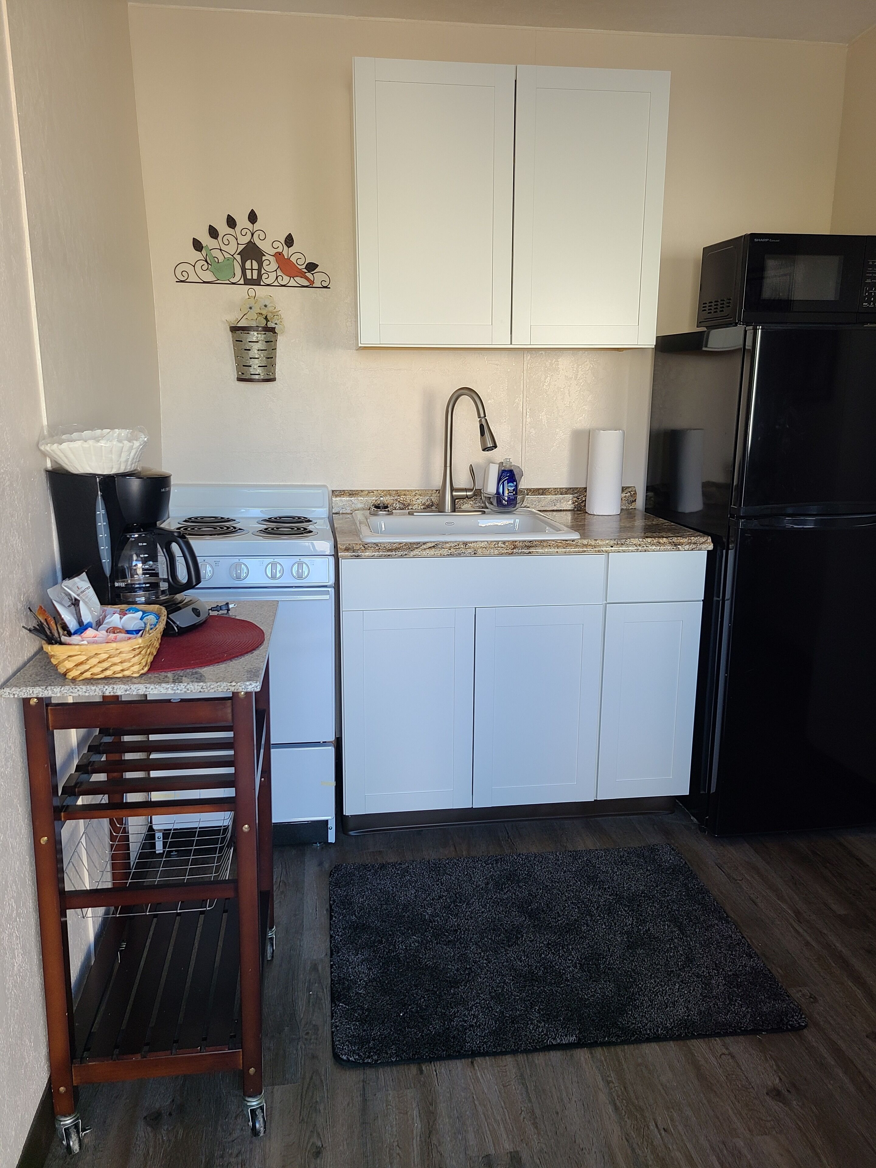 A compact kitchen with white cabinets, a stainless steel sink, a black refrigerator, and a microwave.