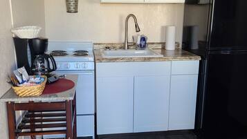 A compact kitchen with white cabinets, a stainless steel sink, a black refrigerator, and a microwave.