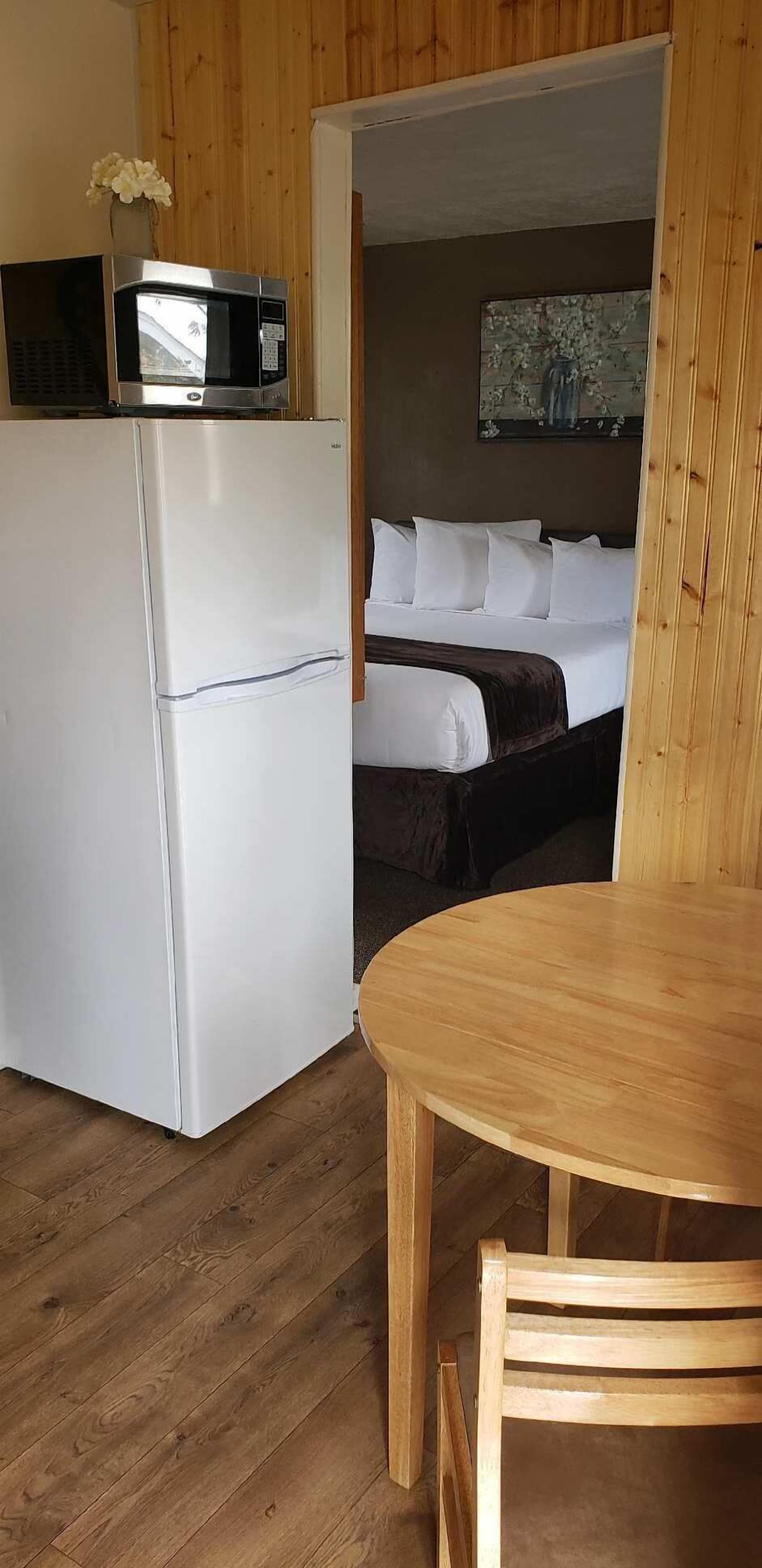 Een knus kamertje met een bed, een kleine kitchenette en een houten eettafel.