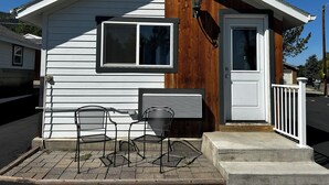 A small, single-story house with a white exterior and a wooden section on the right. There is a front door, a window, and two metal chairs on the porch. - Lamplighter Cabins & Suites (Helena)