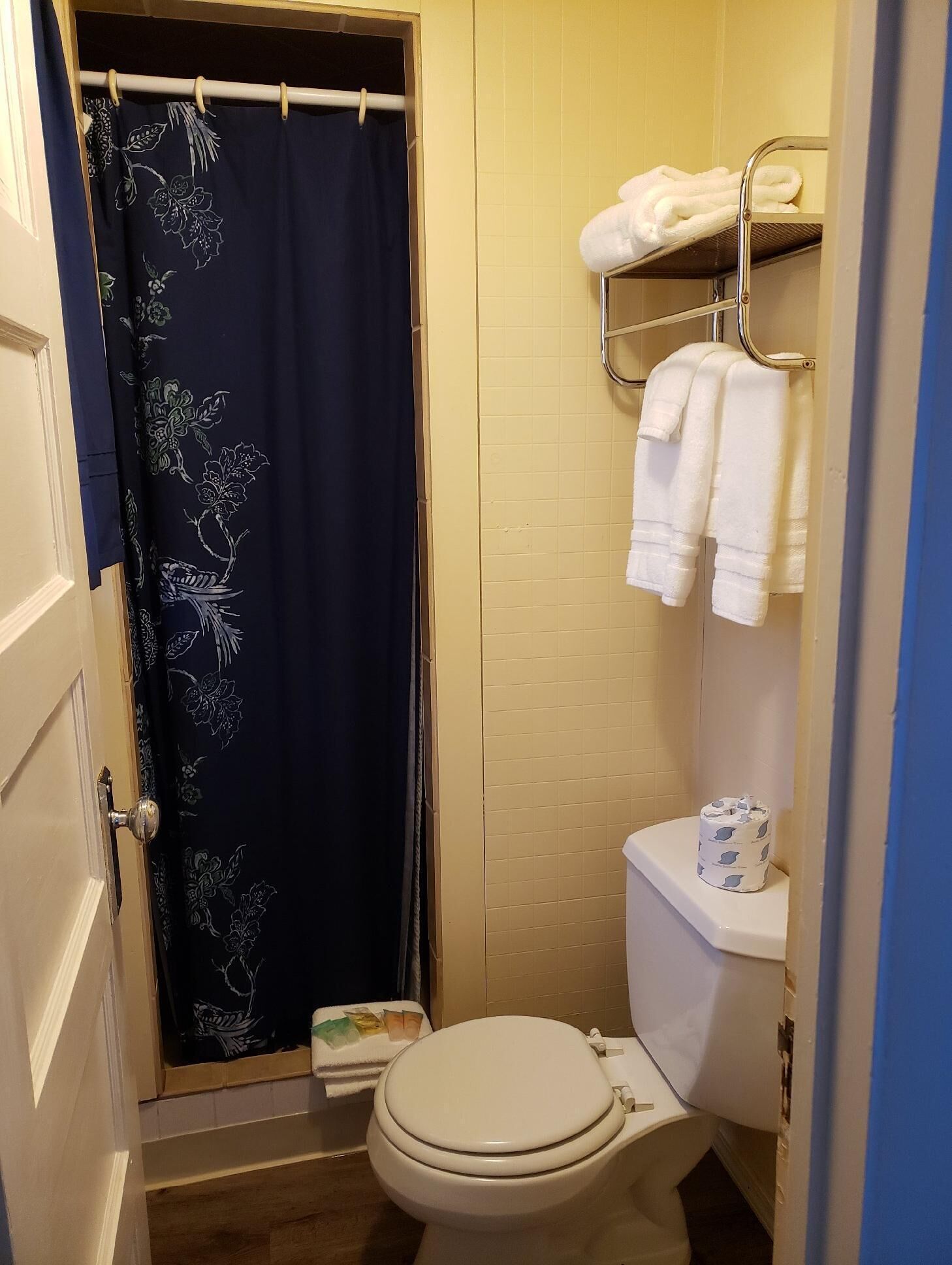 Une petite salle de bain avec des toilettes, un rideau de douche orné de motifs floraux et un porte-serviettes avec des serviettes.