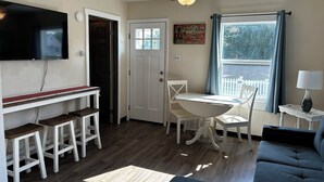 A compact living space with a dining area, a sofa, a ceiling fan, a TV mounted on the wall, and a window with curtains. - Lamplighter Cabins & Suites (Helena)