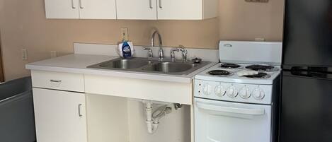 A kitchen with white cabinets, a double sink, a stove, and a refrigerator.