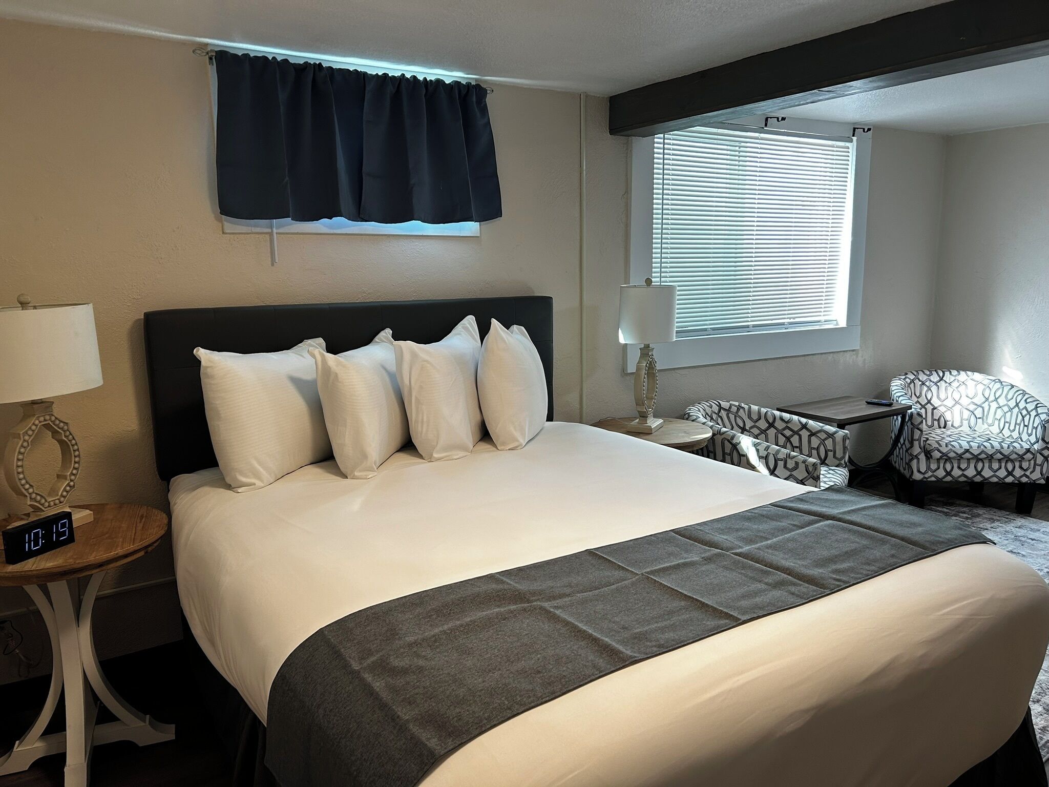 A hotel room with a large bed, a nightstand with a lamp, a chair, and a window with blinds.