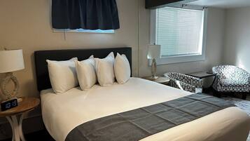 A hotel room with a large bed, a nightstand with a lamp, a chair, and a window with blinds.