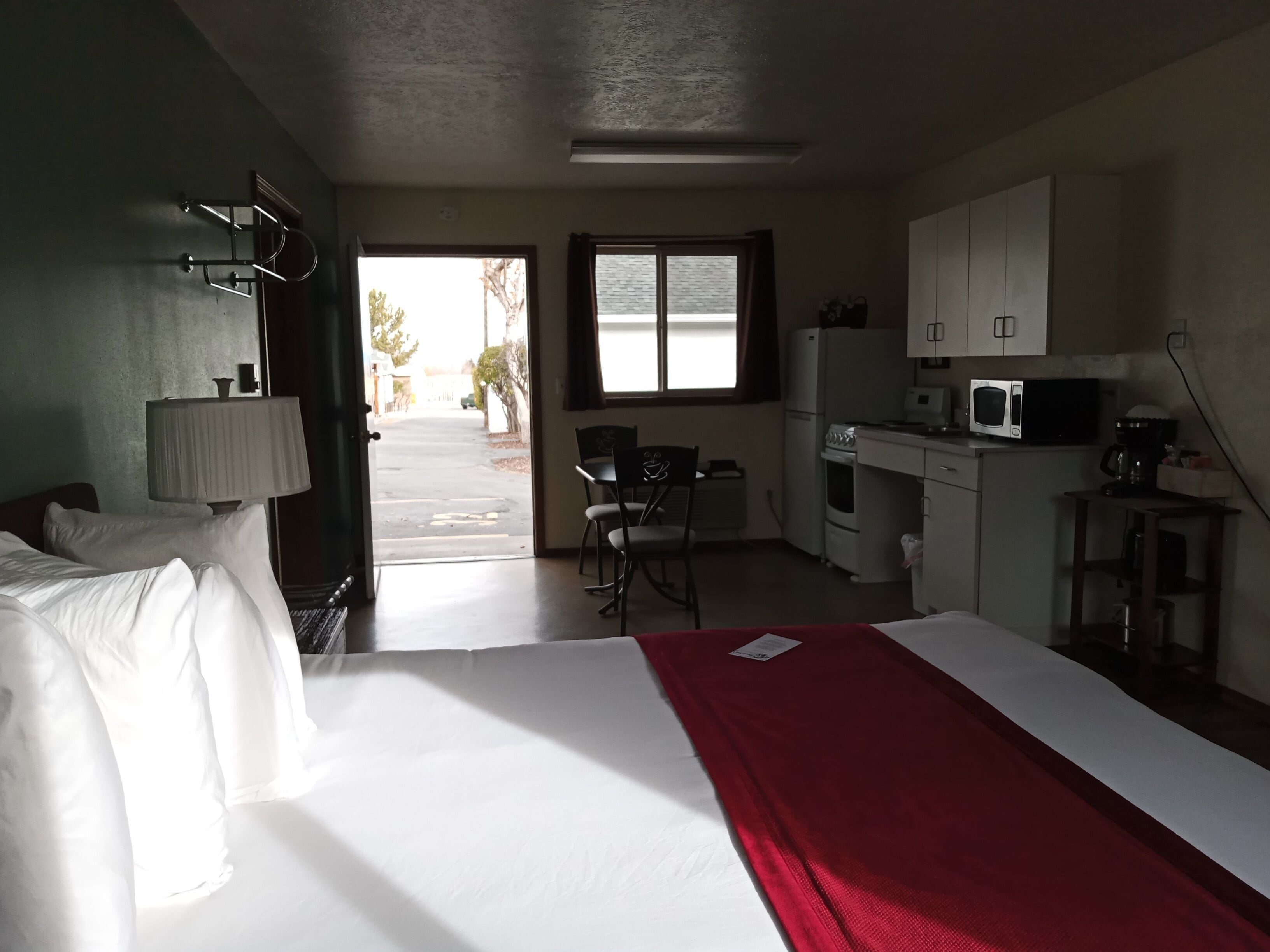 A hotel room with a bed, a desk, a chair, a microwave, and a kitchenette.