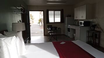 A hotel room with a bed, a desk, a chair, a microwave, and a kitchenette.