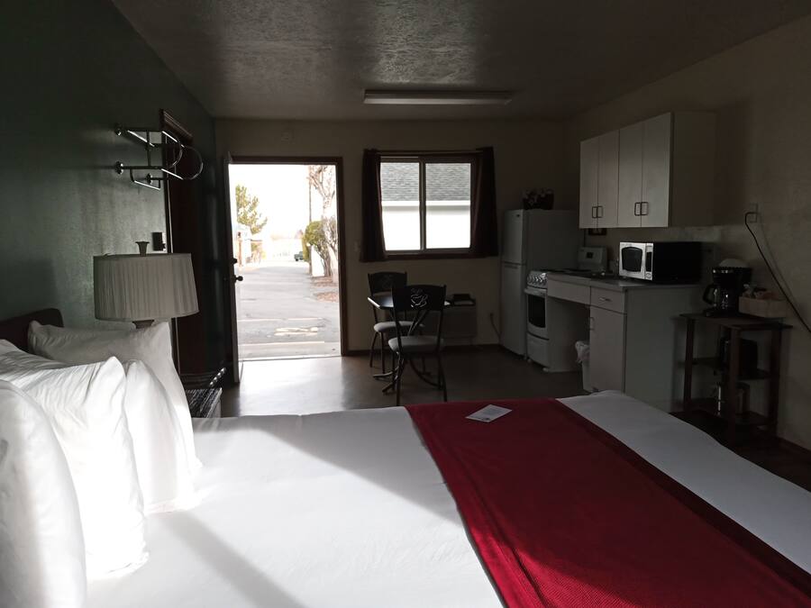 A hotel room with a bed, a desk, a chair, a microwave, and a kitchenette.