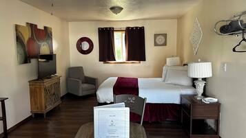 A hotel room with a bed, a desk, a chair, a TV, and a window with curtains.