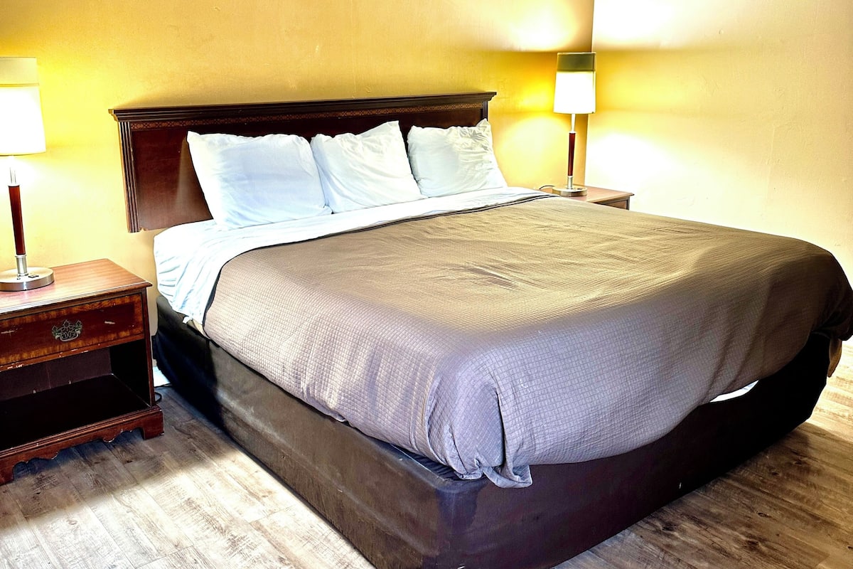 A hotel room with a large bed, two bedside tables, and a wooden floor.