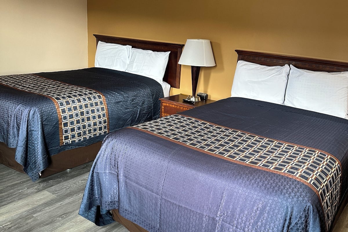 A hotel room with two beds, each with a patterned bedspread and white pillows.