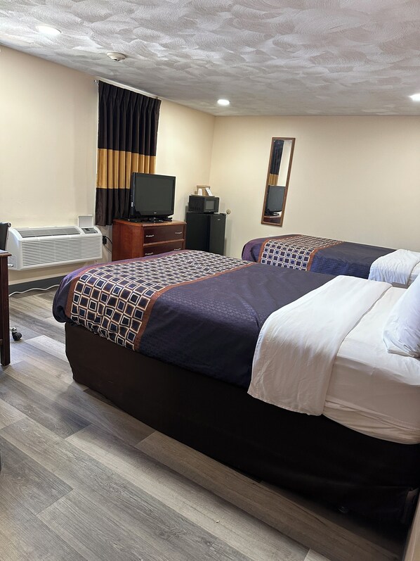 Habitación de hotel con dos camas, un televisor, un refrigerador pequeño y un aire acondicionado, además de un espejo en la pared.