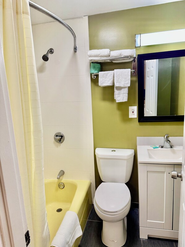 Een badkamer met een geel bad, een wit toilet en een wastafel met een spiegel erboven.