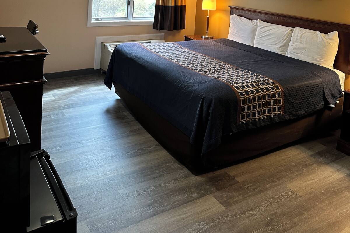 A hotel room with a bed, a desk, a lamp, and a window with curtains.