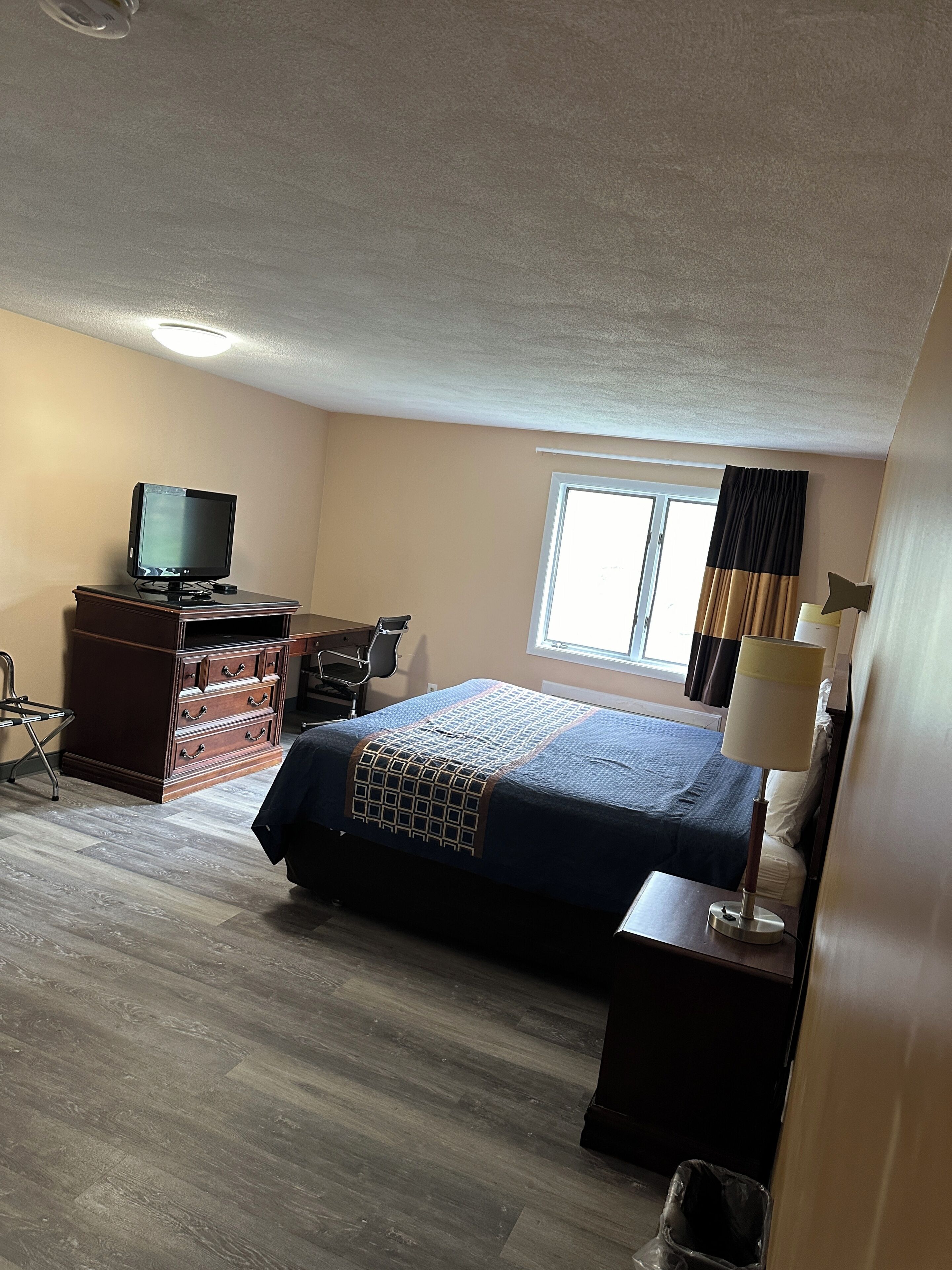 A hotel room with a bed, dresser, television, and a window with curtains.