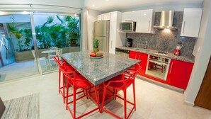 A modern kitchen with red and white cabinets, a granite countertop, and a dining area with red chairs. - In heart of town 1BR condo in steps distance from the 5th Av by Happy Address (Playa del Carmen)