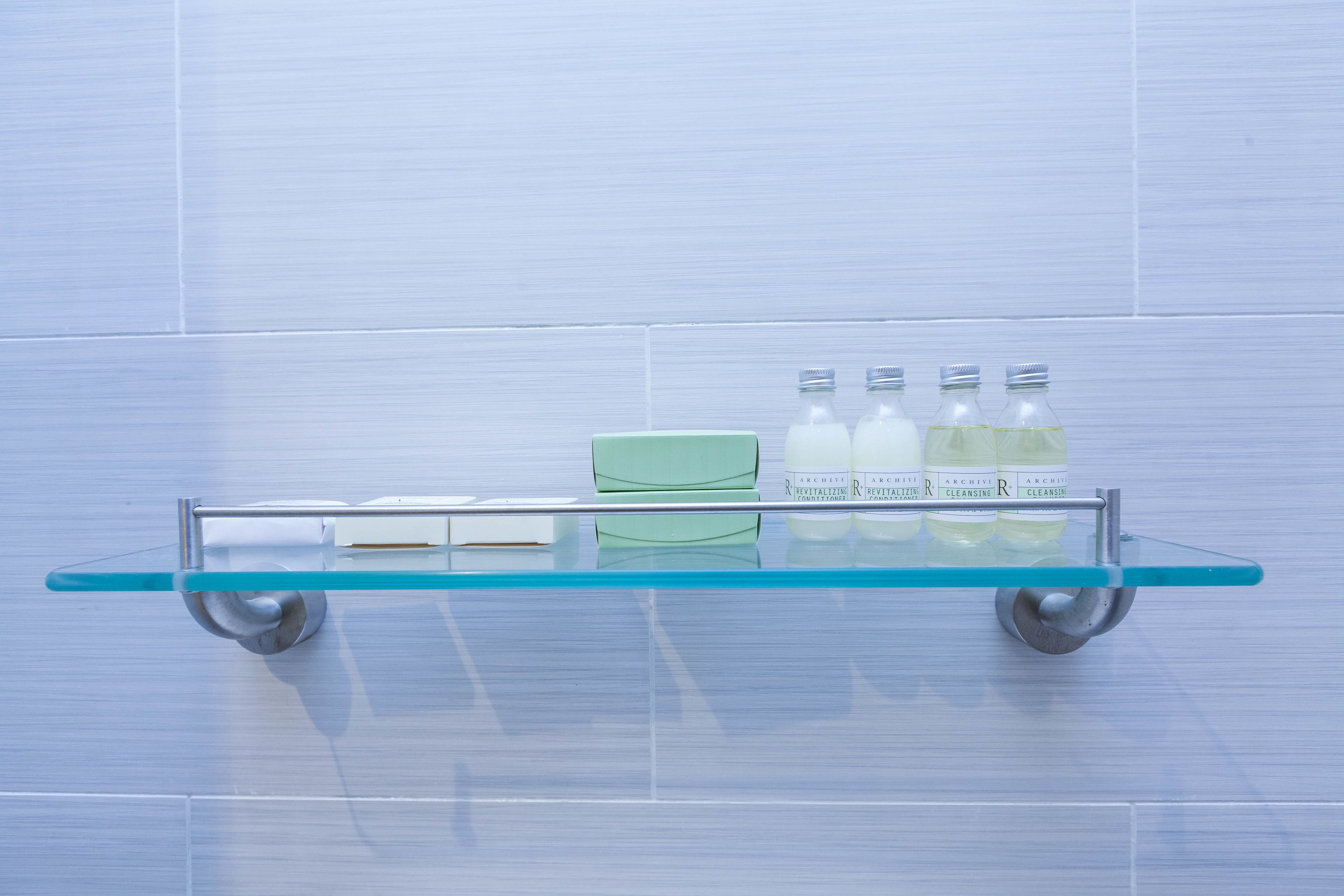 Una repisa de vidrio con una caja verde y cuatro botellas de Archie Cleansing R sobre una pared de azulejos.