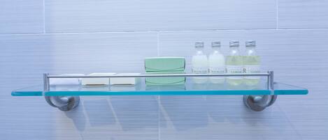 Una repisa de vidrio con una caja verde y cuatro botellas de Archie Cleansing R sobre una pared de azulejos.