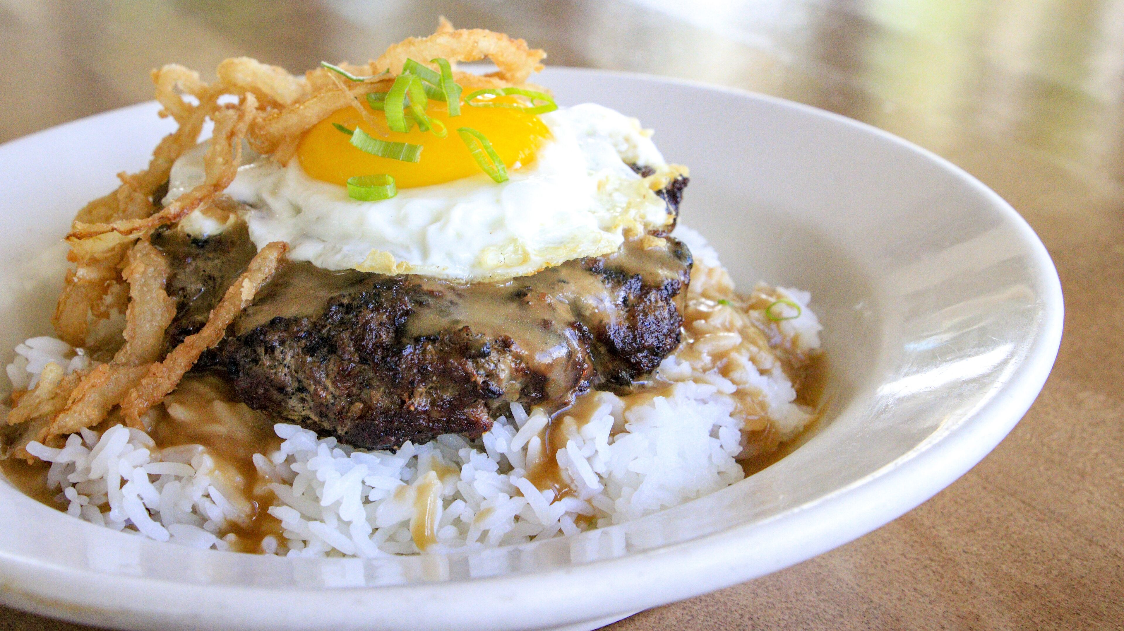 A plate of food with rice, a fried egg, and a piece of meat topped with fried onions.
