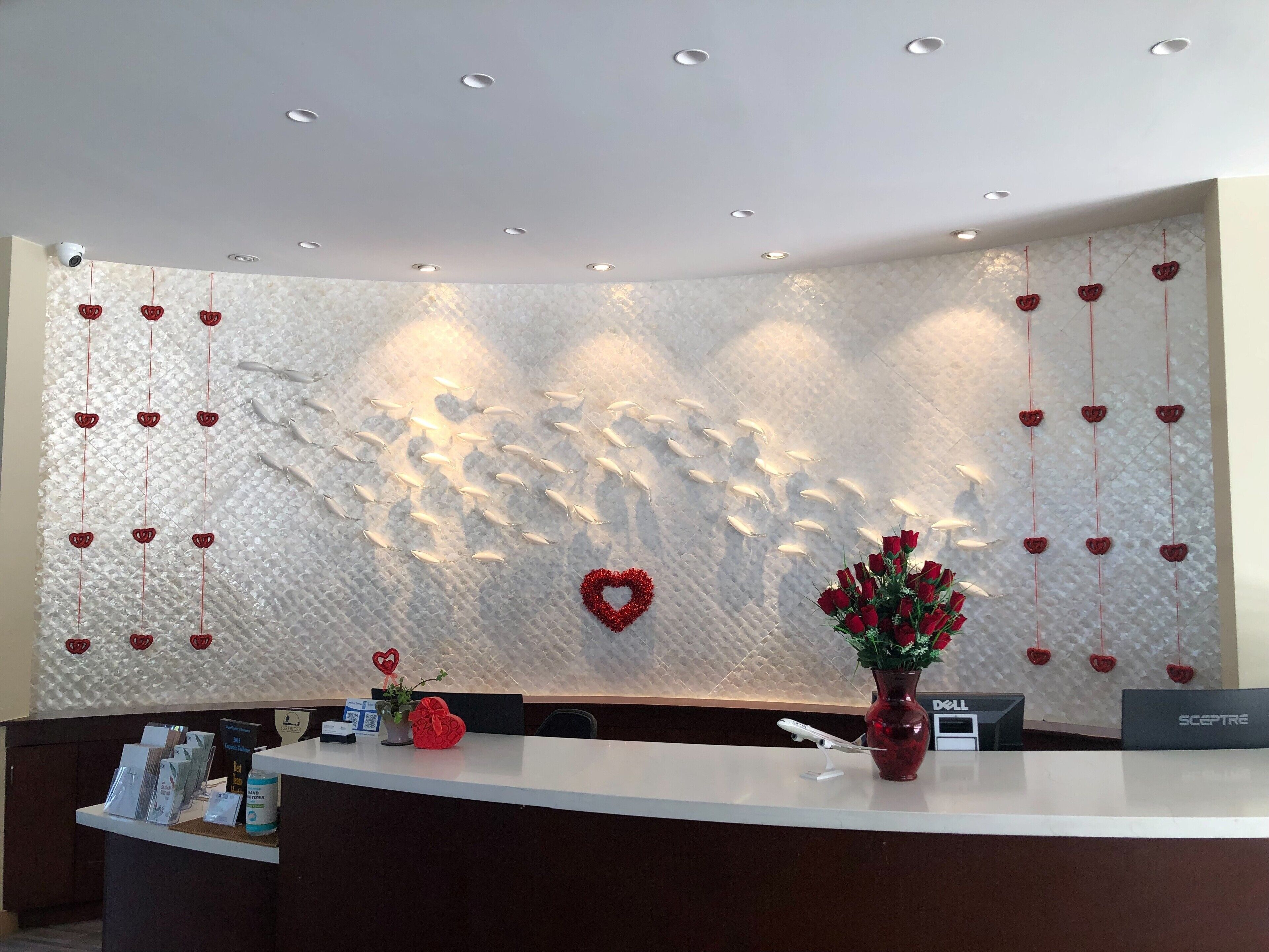 A reception desk with a white countertop, a vase with red roses, and a heart-shaped decoration on the wall.