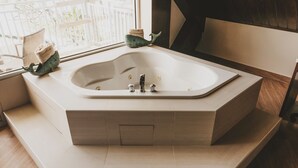 A modern bathroom with a freestanding bathtub, wooden steps, and a window with a view of buildings. - Surfrider Resort Hotel (Saipan)
