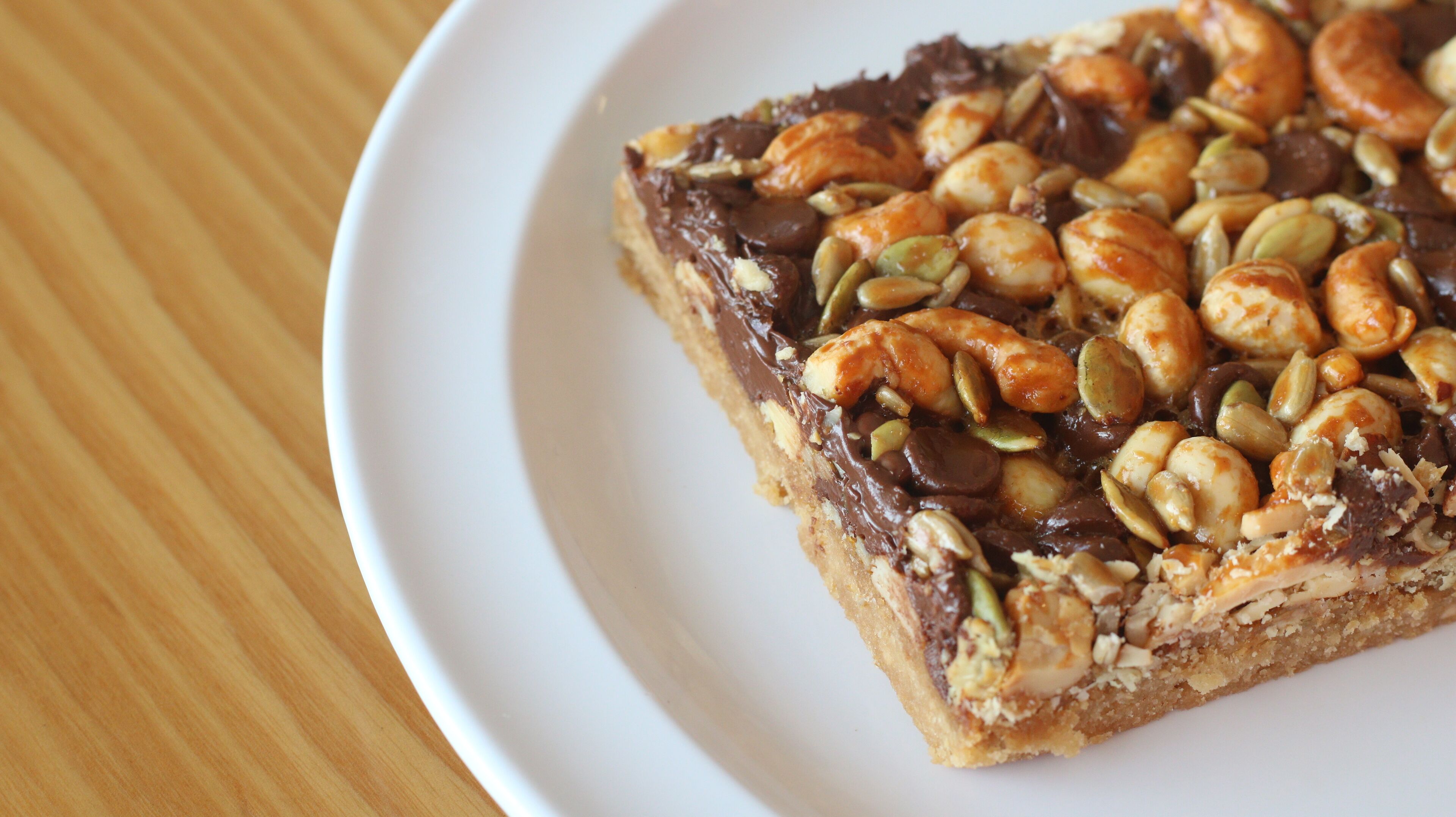 Une part de dessert garnie de noix et de chocolat, présentée sur une assiette blanche.