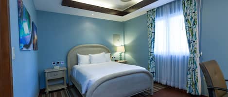 Una habitación de hotel con cama, mesita de noche, silla, ventilador de techo y ventana con cortinas.