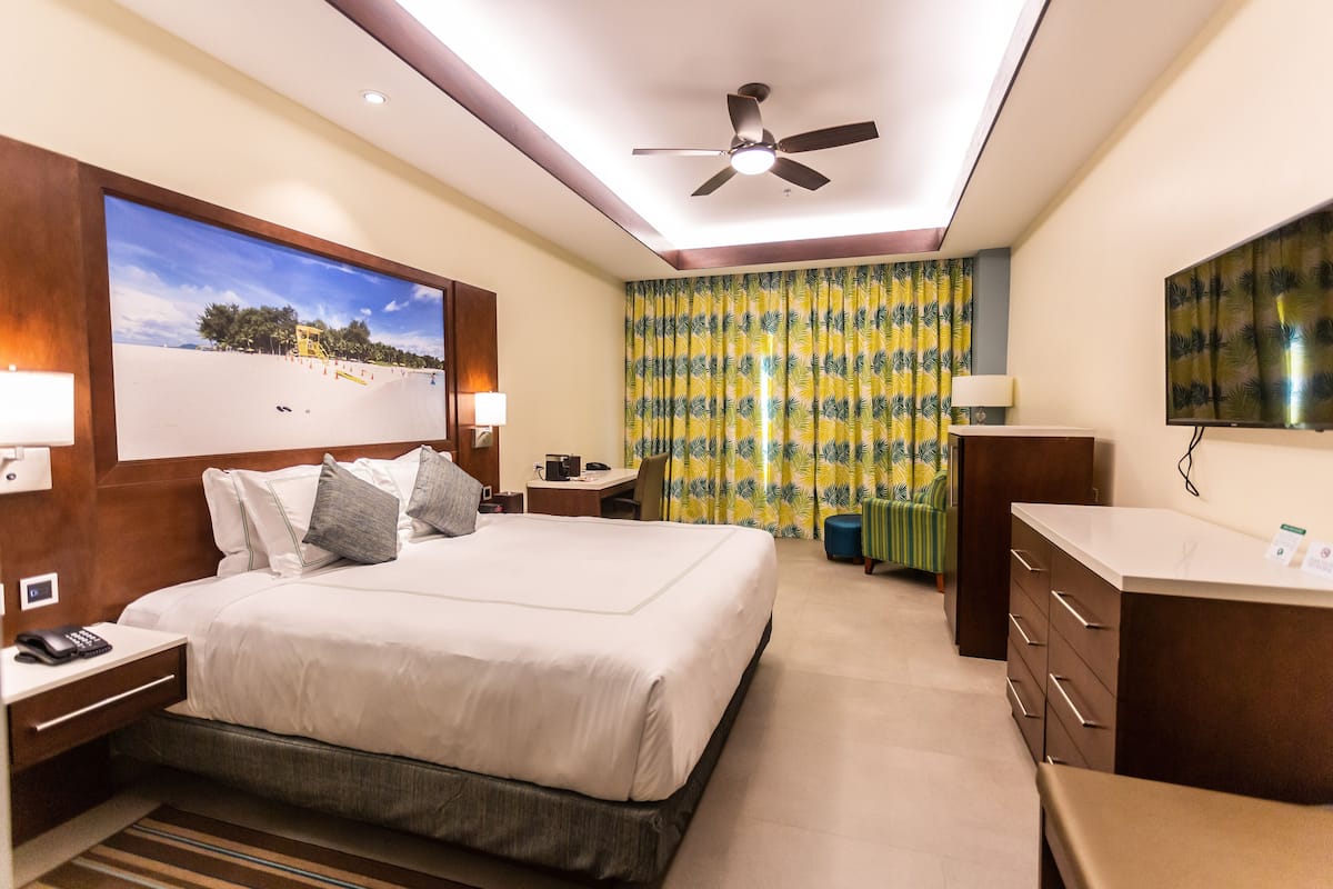 A hotel room with a bed, a desk, a chair, a TV, and a ceiling fan.