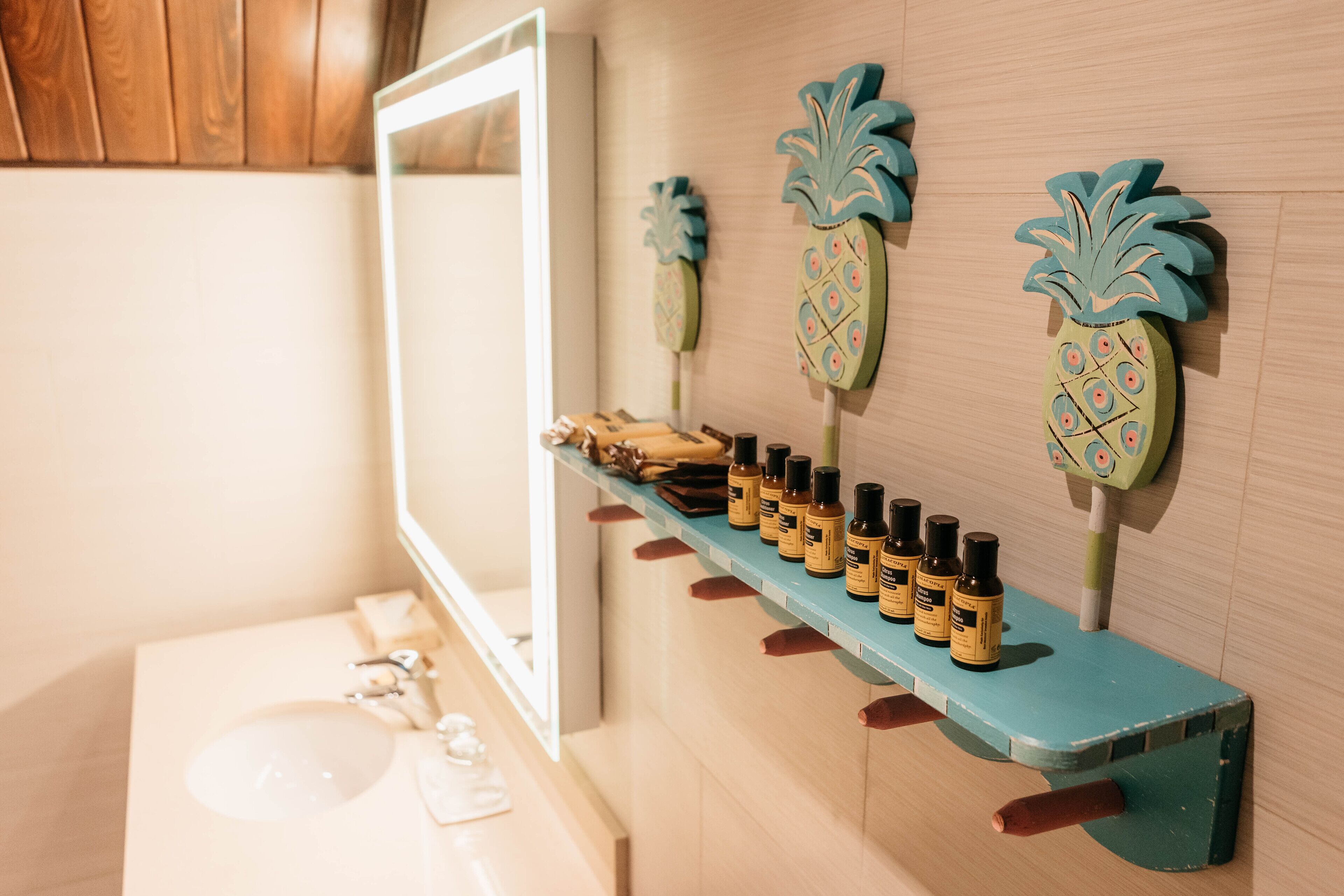 A bathroom with a wooden vanity, a mirror, and a shelf with bottles.