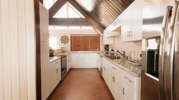 A modern kitchen with white cabinets, stainless steel appliances, and a wooden ceiling.
