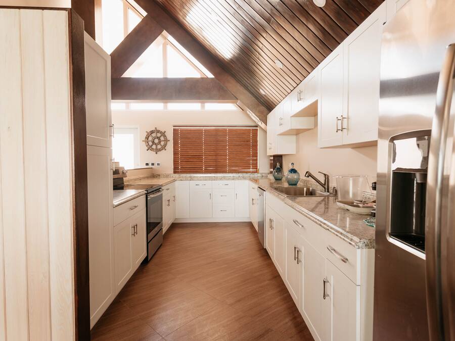 A modern kitchen with white cabinets, stainless steel appliances, and a wooden ceiling.