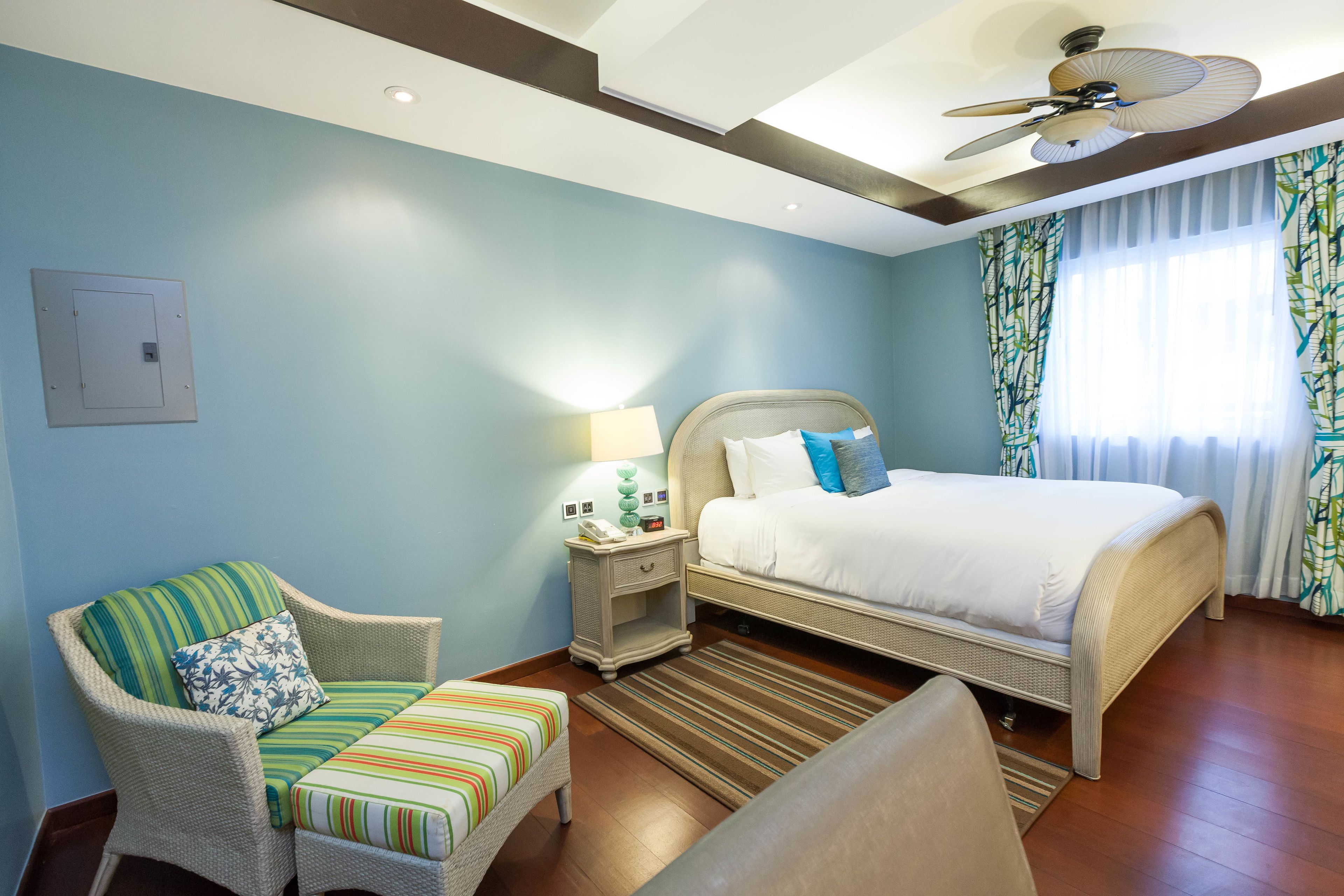 Une chambre d’hôtel avec un lit, une chaise, une table de chevet et un ventilateur de plafond.