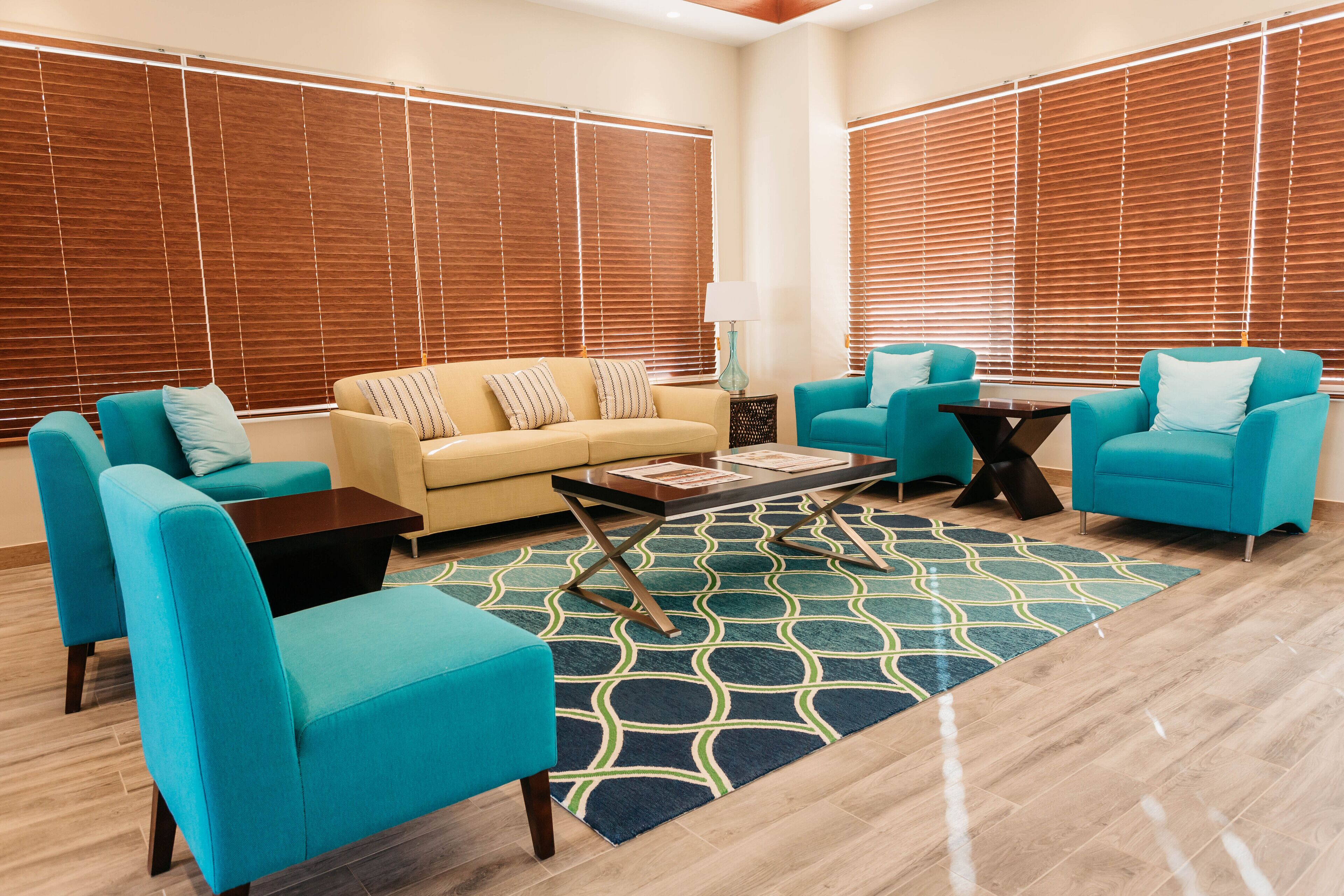A modern living room with a beige sofa, teal armchairs, a coffee table, and a patterned rug.