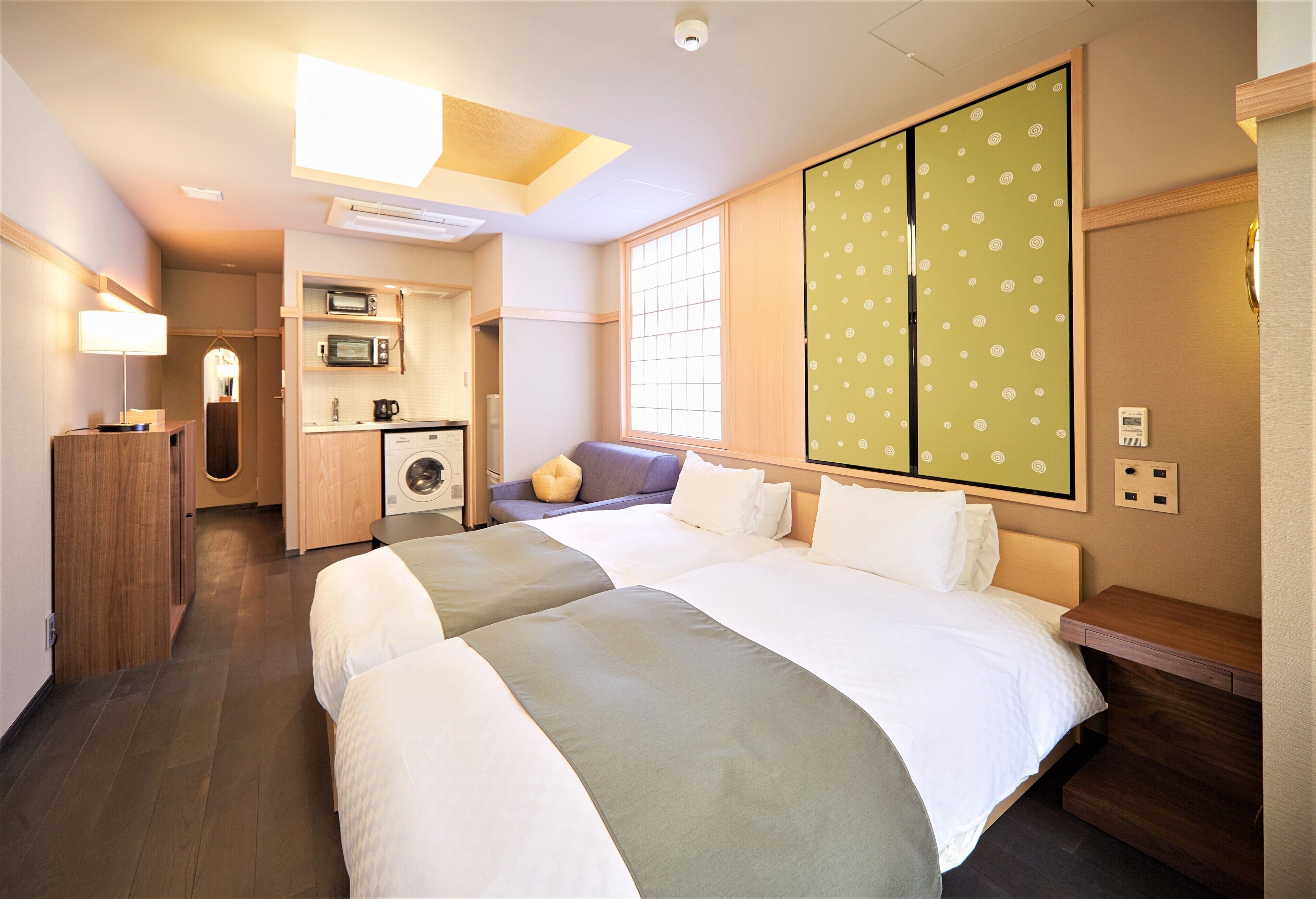 Ein Hotelzimmer mit zwei Betten, einer Küchenzeile, einer Waschmaschine und einer Schiebetür mit Punkten.