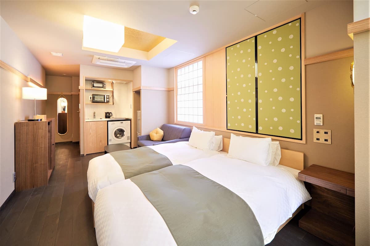 A hotel room with two beds, a kitchenette, a washing machine, and a sliding door with a polka dot pattern.