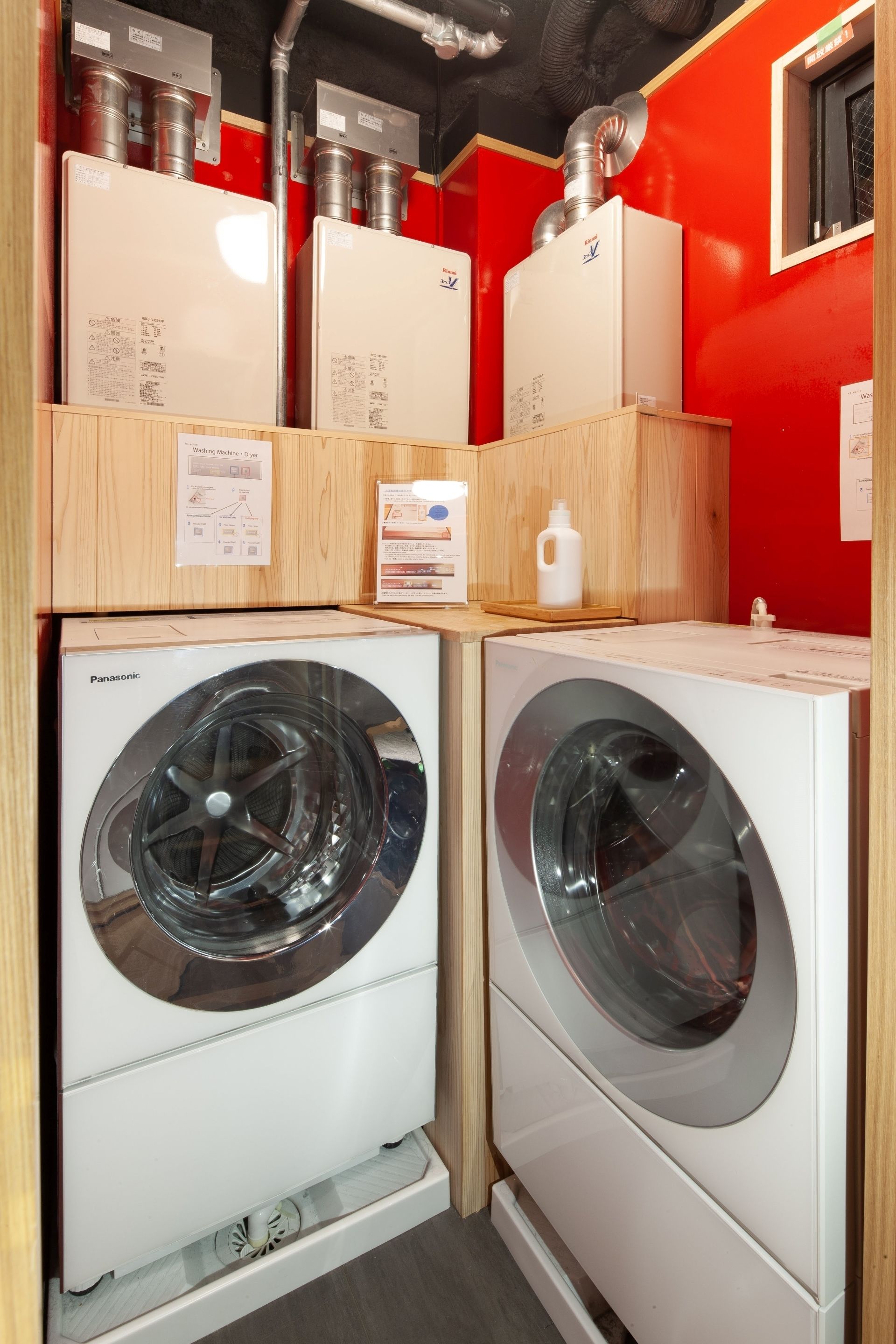 Une buanderie avec deux machines à laver blanches, un meuble en bois et un mur rouge.