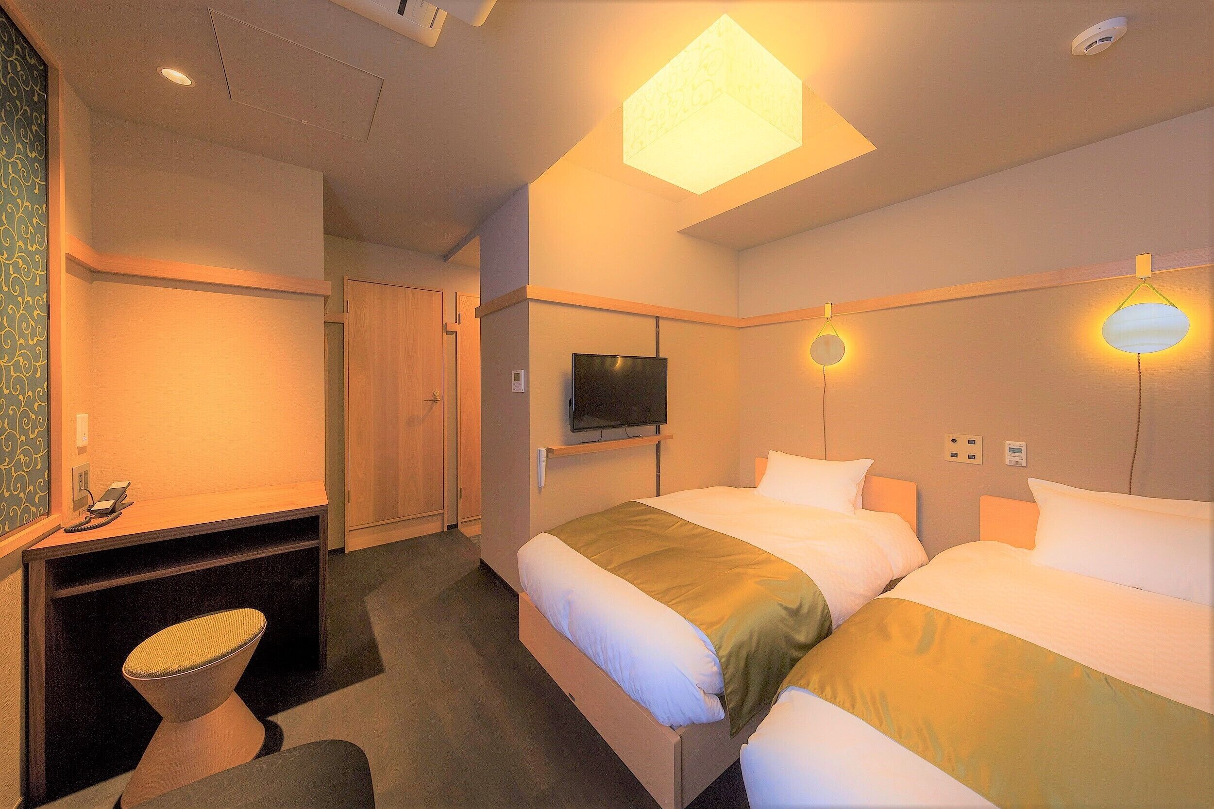Ein Hotelzimmer mit zwei Betten, einem Fernseher, einem Schreibtisch mit Stuhl und einer Schreibtischlampe.
