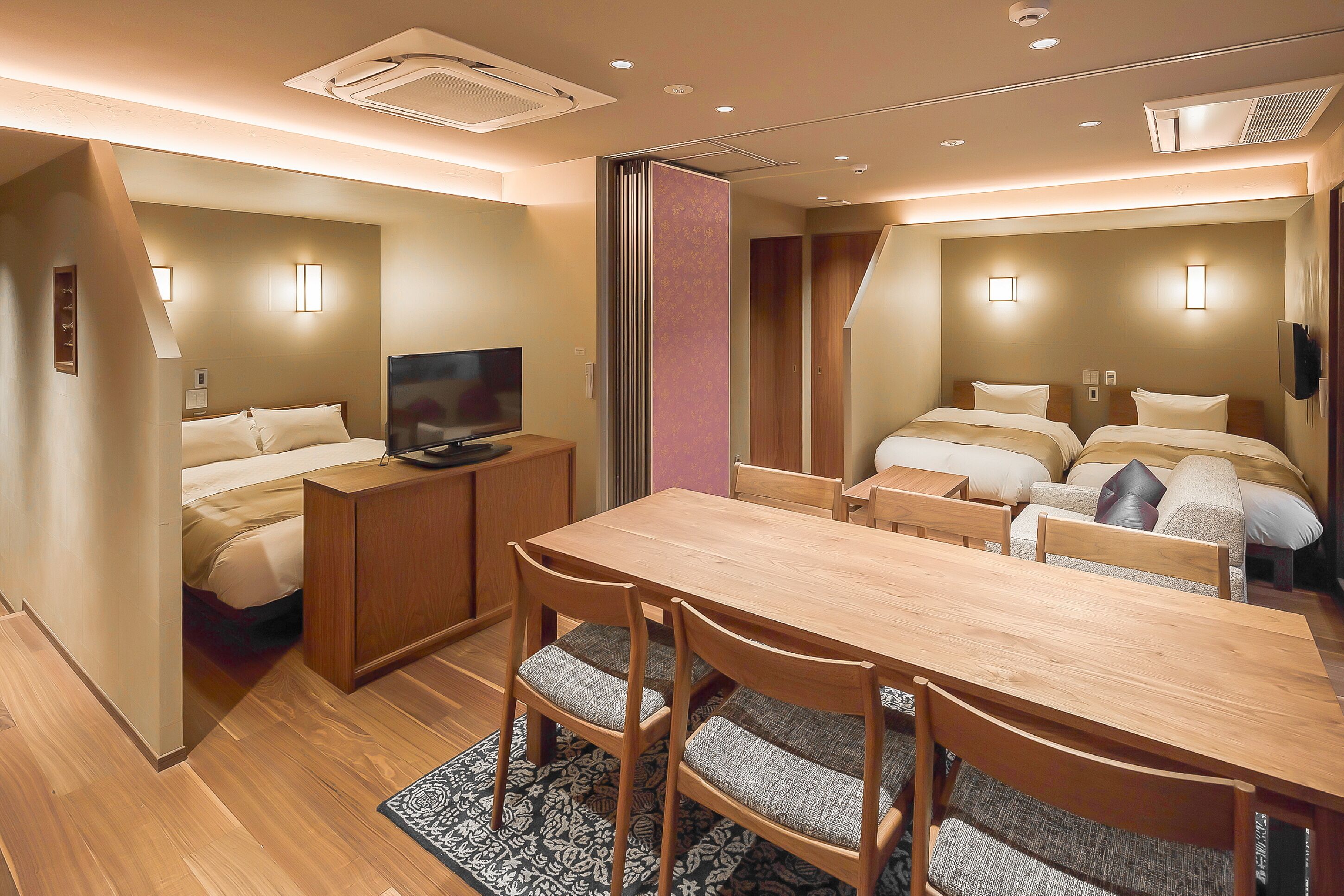 Ein Hotelzimmer mit Holztisch, zwei Betten, einem Fernseher und einem Kleiderschrank.