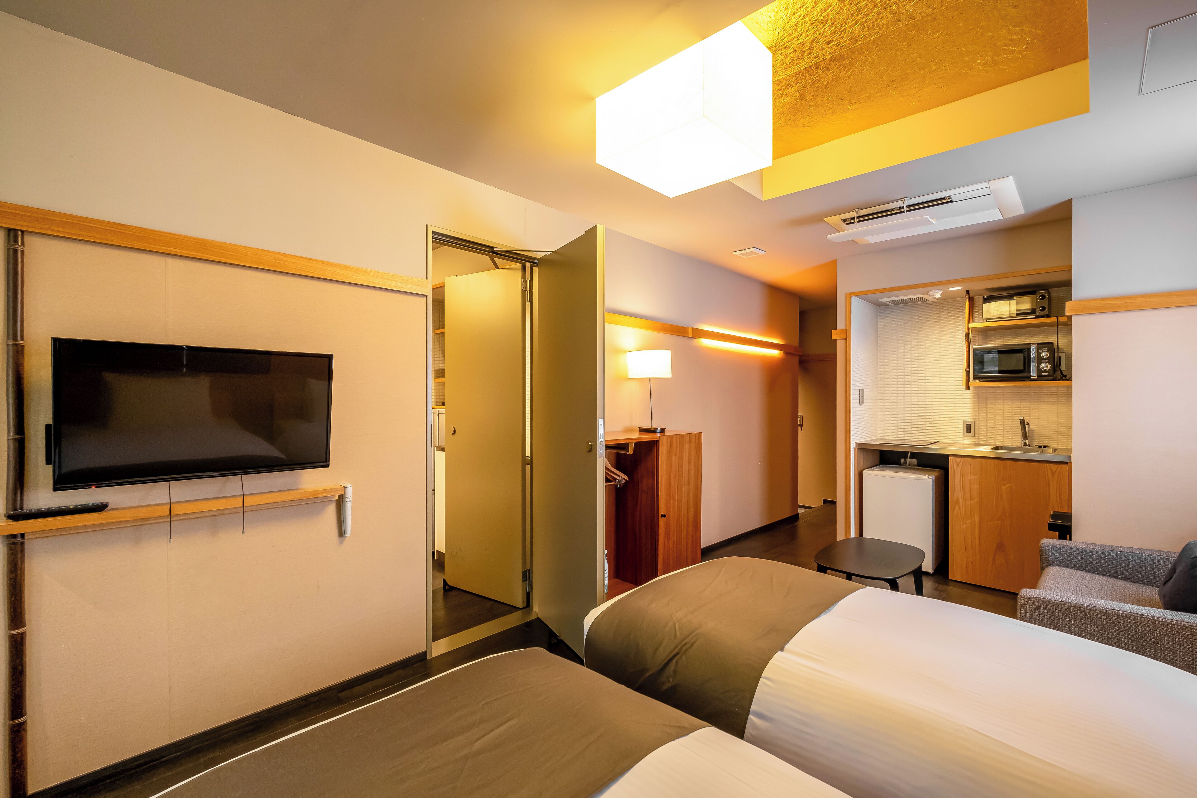 A hotel room with a TV, a bed, a desk, a chair, and a kitchenette.