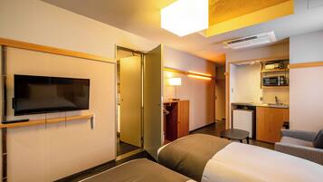 A hotel room with a TV, a bed, a desk, a chair, and a kitchenette.