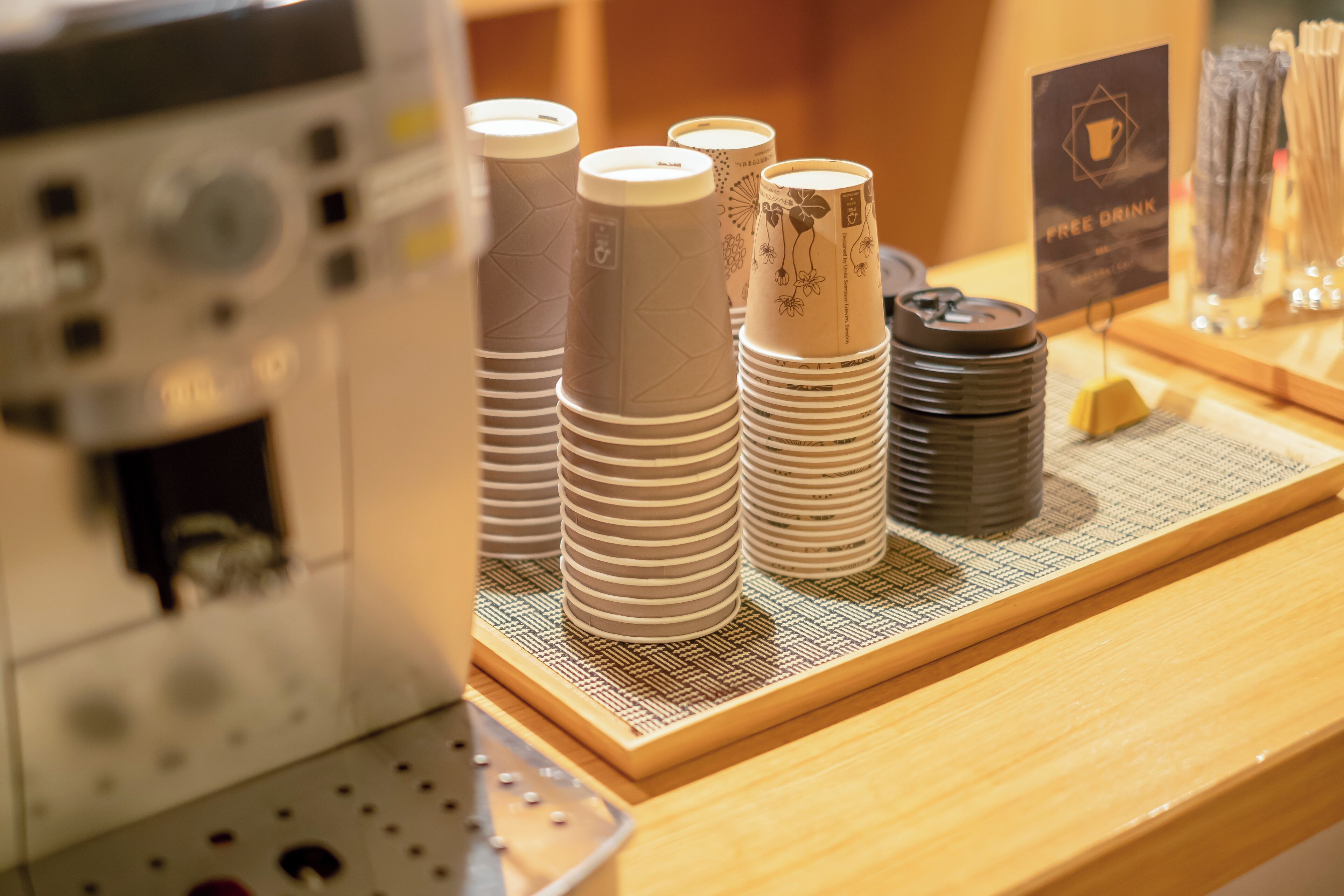Stacks of disposable cups and a coffee machine on a counter.
