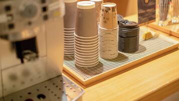 Stacks of disposable cups and a coffee machine on a counter.