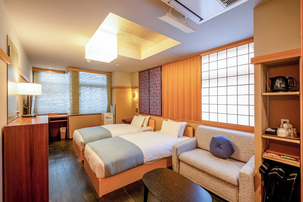 A hotel room with two beds, a desk, a chair, a sofa, and a wardrobe.