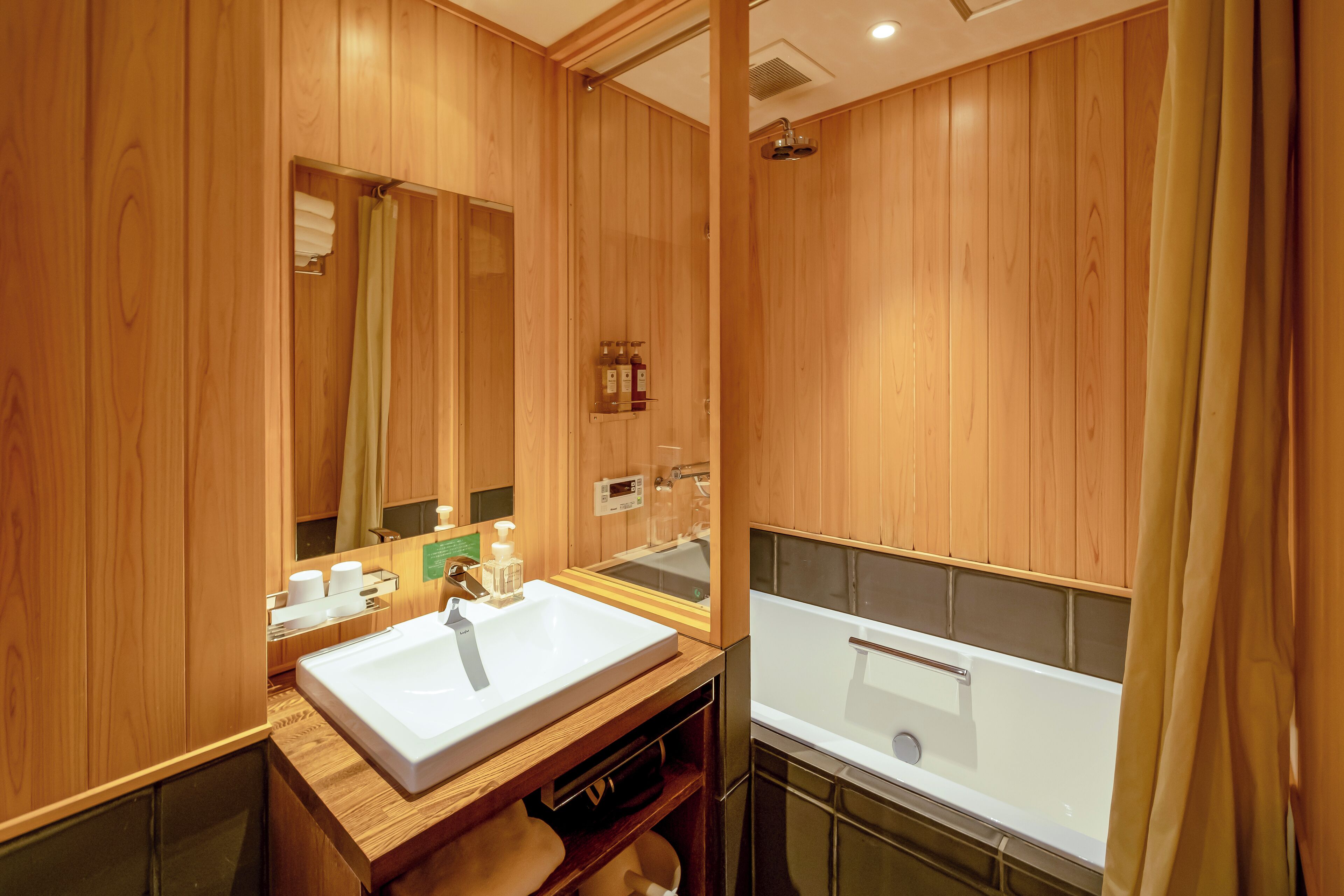A wooden-paneled bathroom with a sink, mirror, and shower.
