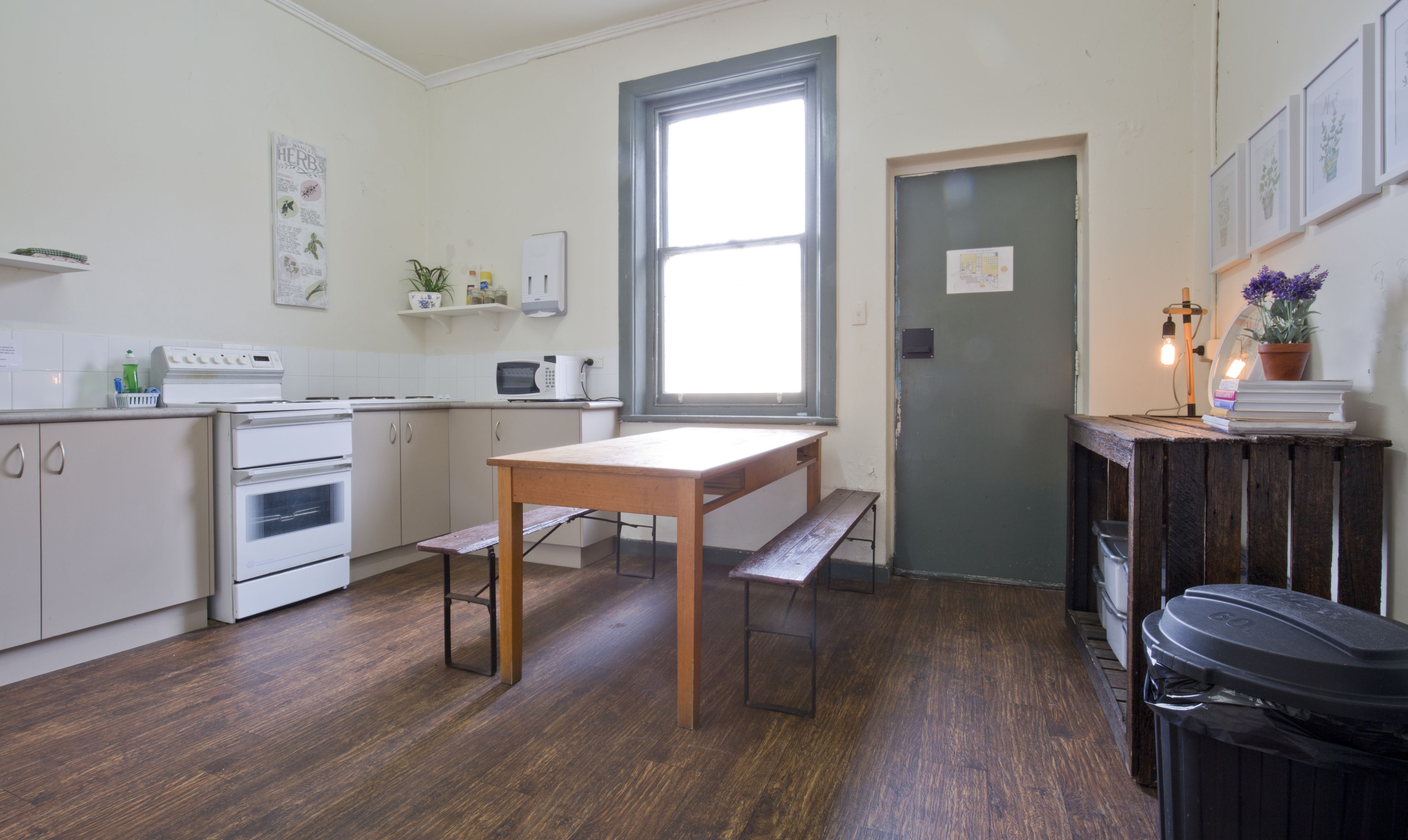 A compact kitchen with white appliances, a wooden table, and a bench.