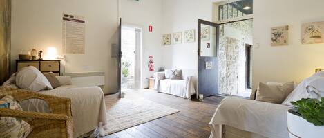 Una habitación con dos camas, una silla de mimbre, una mesita con una lámpara y un extintor en la pared.