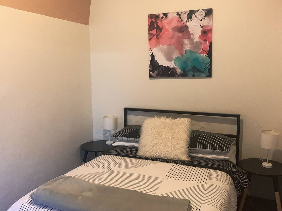 A neatly arranged bedroom with a bed, bedside tables, and a wall-mounted abstract painting.