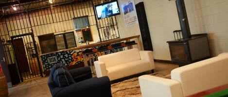 A lounge area with a white sofa, a black sofa, and a green pool table. There is a television mounted on the wall and a fireplace.